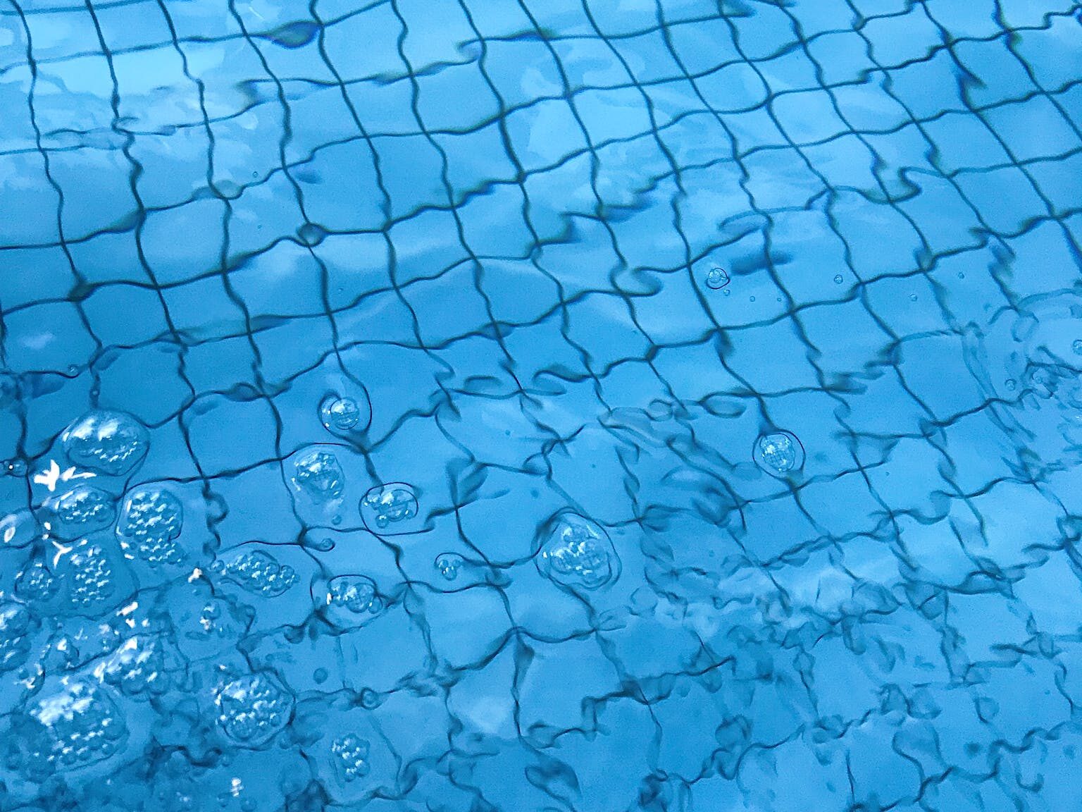 From above of transparent clean water of swimming pool with ceramic bottom in daylight